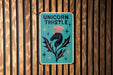 a sign on a wooden wall that says unicorn thistle