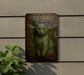 a green cat sitting on top of a metal plaque