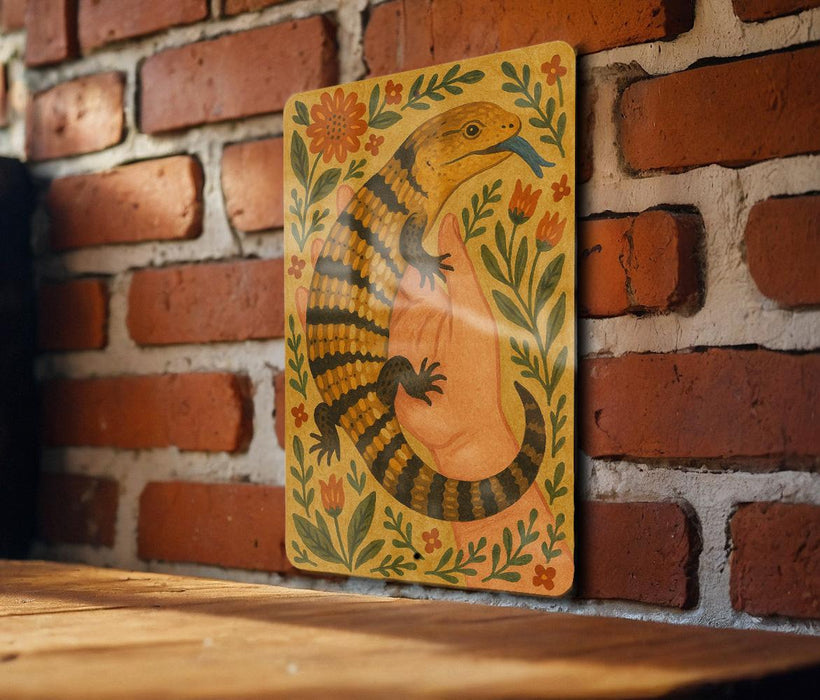 a colorful illustration of a lizard or salamander, with a floral design surrounding it, mounted on a brick wall.