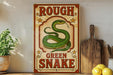 a vintage-style sign with a green snake on it, placed on a wooden surface next to a wooden cutting board and some lemons.