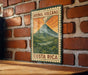 A vintage-style metal sign with the text "ARENAL VOLCANO" and "COSTA RICA" is displayed on a brick wall.