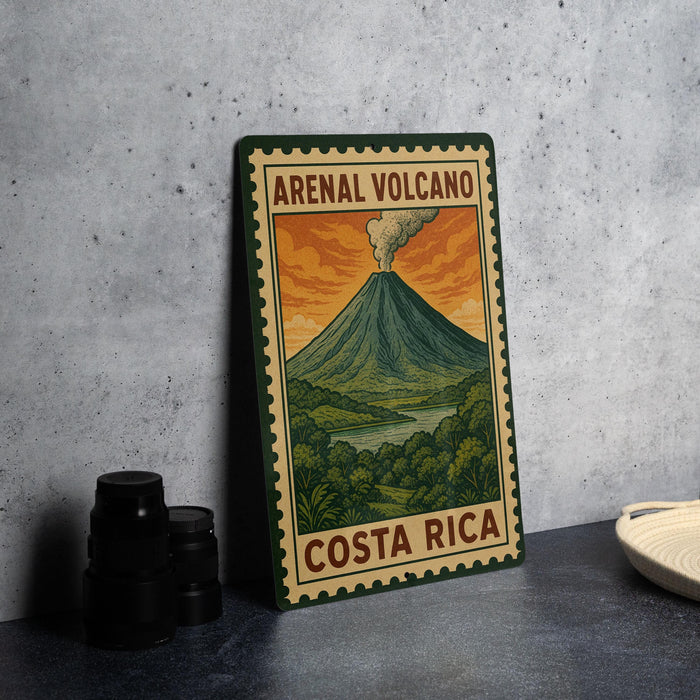 A framed illustration of a volcano with the text "ARENA VOLCÓNO" and "COSTA RICA" on it, placed on a table next to some black camera lenses.