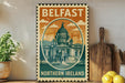 A vintage-style metal sign with the text "Belfast Northern Ireland" and an illustration of a building, placed on a wooden surface next to a potted plant and a wooden cutting board.
