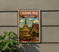 A vintage-style metal sign with a temple illustration and the text "CHIANG MAI THAILAND" displayed on a wall.