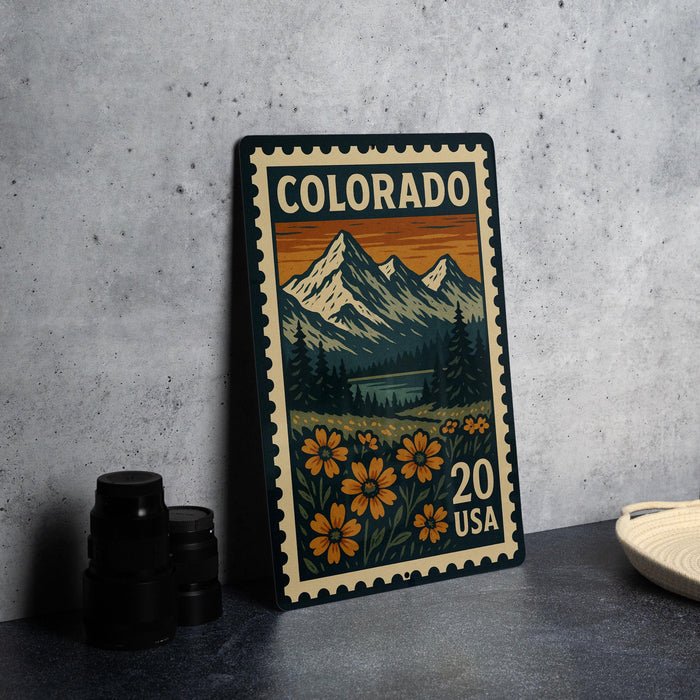 A colorful postage stamp from Colorado, featuring a mountain landscape with flowers, is displayed on a table.