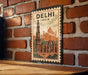 A vintage-style metal poster depicting the Taj Mahal and the Qutub Minar, with the text "DELHI INDIA" prominently displayed.