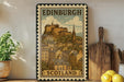 A vintage-style metal sign depicting the Edinburgh Castle in Scotland, with a wooden board and a potted plant in the foreground.