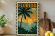 A framed vintage-style stamp depicting a tropical beach scene with palm trees, a sunset, and a body of water.
