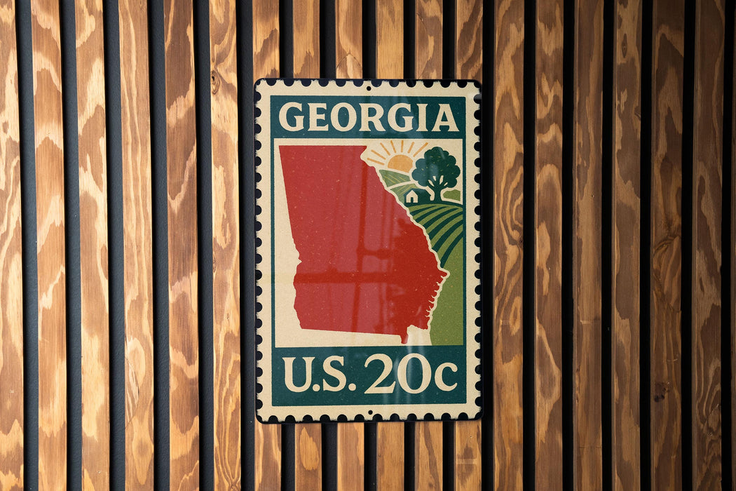 A U.S. postage stamp from Georgia, featuring a red state outline and a green field, is displayed on a wooden wall.