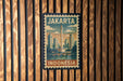 A vintage-style postage stamp from Indonesia featuring a cityscape and a bridge, mounted on a wooden wall.