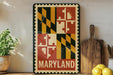A framed sign displaying the state of Maryland, featuring the state's flag design, is displayed on a shelf next to a wooden cutting board and some lemons.