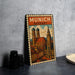 A vintage metal poster of the city of Munich, Germany, featuring the city's iconic landmarks such as the Brandenburg Gate and the Brandenburg Cathedral.