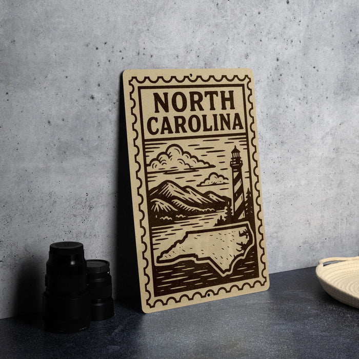 a wooden sign with the text "NORTH CAROLINA" and a lighthouse illustration, placed on a countertop next to some black camera lenses.