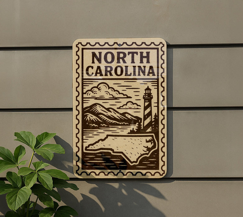 a sign with the text "NORTH CAROLINA" and a lighthouse illustration, mounted on a wall next to a plant.
