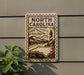 a sign with the text "NORTH CAROLINA" and a lighthouse illustration, mounted on a wall next to a plant.