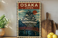 A framed poster of Osaka, Japan, featuring a traditional Japanese castle or pagoda with a bridge in the background.