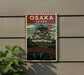 A vintage-style poster of Osaka, Japan, featuring a castle-like structure and a bridge, is displayed on a wall.