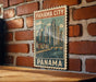 A vintage-style poster of Panama City, featuring a cityscape with a bridge and water, is displayed on a brick wall.