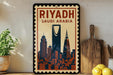 A vintage-style poster of Riyadh, Saudi Arabia, featuring the city's skyline and landmarks, is displayed on a wall next to a wooden cutting board and a potted plant.