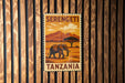 A vintage-style postage stamp from Tanzania featuring an elephant in a grassy field with mountains in the background.