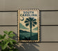 A decorative metal sign with the text "SOUTH CAROLINA" and a palm tree illustration, mounted on a wall.