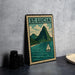 A framed illustration of St. Lucia, featuring a mountain landscape with a sailboat on the water, is displayed on a table.