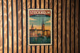 A vintage-style poster of Stockholm, Sweden, featuring a cityscape with a church spire and a river, is displayed on a wooden wall.