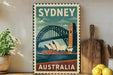 A vintage-style poster of Sydney, Australia, featuring the iconic Sydney Harbour Bridge and the Sydney Opera House, is displayed on a wall next to a wooden cutting board and some potted plants.