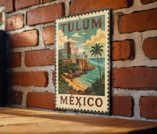 A vintage-style metal sign with the text "TULUM MEXICO" is displayed on a brick wall, featuring a tropical beach scene with palm trees and a castle.