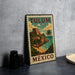A vintage-style metal sign with the text "TULUM MEXICO" and an illustration of a tropical beach and castle, placed on a gray countertop next to some black camera lenses.