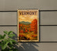 A vintage-style postage stamp depicting a scenic autumn landscape in Vermont, with a red barn and a winding road in the foreground.
