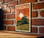 A vintage-style metal sign with the word "VIRGINIA" prominently displayed, featuring a landscape with a mountain, field, and sunset.