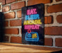 A neon sign on a brick wall that reads "EAT. SLEEP. ARCAKE. REPEAT" with a joystick icon below it.
