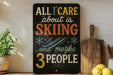A black sign with colorful text that reads "ALL I CARE about is SKIING...and maybe 3 people" is displayed on a wooden shelf next to a wooden cutting board and a potted plant.