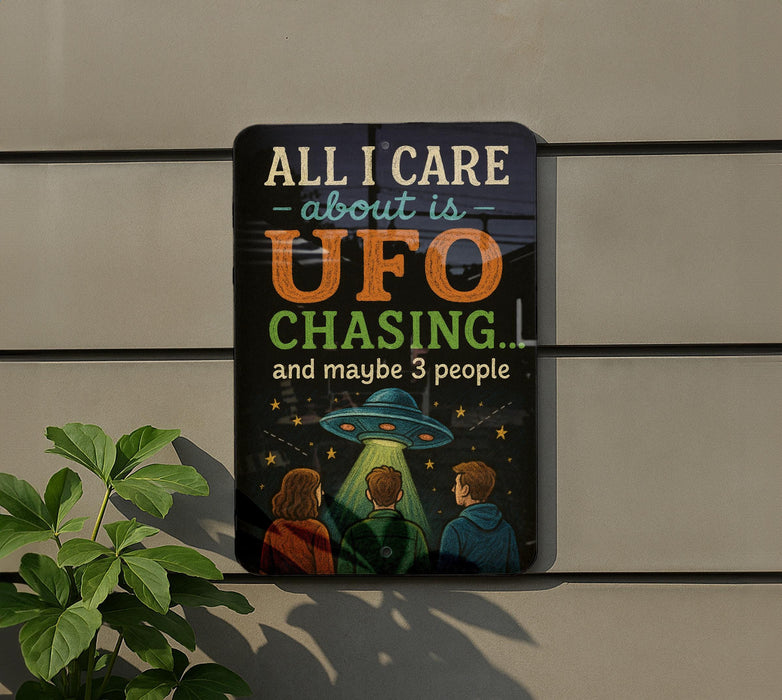 a sign with a humorous message about UFO chasing, accompanied by an illustration of three people looking up at an alien spacecraft.