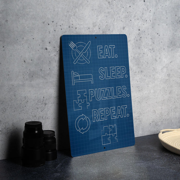 a blue sign with white text that reads "EAT. SLEEP. PUZZLES. REPEAT." The sign is placed on a gray countertop next to a stack of black cups and a white bowl.