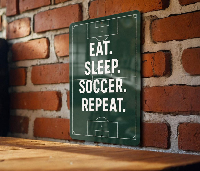 A green sign with white text is mounted on a brick wall, displaying the message "EAT. SLEEP. SOCCER. REPEAT."