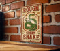 A vintage-style sign with a green snake on a brick wall, featuring the text "ROUGH GREEN SNake" in a decorative font.