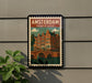 A framed poster of Amsterdam, Netherlands, featuring a colorful illustration of the city's iconic architecture, including a bridge and canal.
