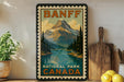 A vintage-style poster of Banff National Park, Canada, featuring a mountain landscape with a lake and pine trees, is displayed on a wall next to a wooden cutting board and some kitchen utensils.