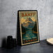 A vintage-style metal stamp depicting a mountain landscape with a lake, surrounded by pine trees, is displayed on a gray countertop next to some black camera lenses.