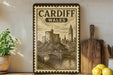 a framed vintage-style illustration of Cardiff, Wales, with a castle and a bridge in the background. The text "CARDIFF WALES" is prominently displayed on the frame.