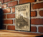 A vintage-style metal sign with the text "CARDIFF WALES" and an illustration of a castle and bridge, mounted on a brick wall.