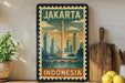 A vintage-style poster of Jakarta, Indonesia, featuring a cityscape with a tall tower, surrounded by a bridge and water, is displayed on a wall next to a wooden cutting board and a potted plant.