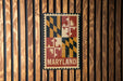 A metal sign with the word "MARYLAND" printed on it, mounted on a wooden wall.