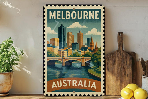 A vintage-style metal stamp depicting the Melbourne skyline, with a bridge and water in the foreground, is displayed on a shelf next to a wooden cutting board and some lemons.