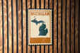 A vintage-style Michigan postage stamp is displayed on a wooden wall.