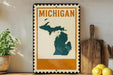 A framed poster of the state of Michigan, featuring a map of the state, is displayed on a shelf next to a wooden cutting board and some lemons.