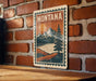 A vintage-style metal sign with the word "MONTANA" prominently displayed, featuring a mountain landscape with a pine tree and a lake.