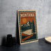 A framed poster of Montana scenery, including mountains, a lake, and a pine tree, is displayed on a countertop next to some black camera lenses.